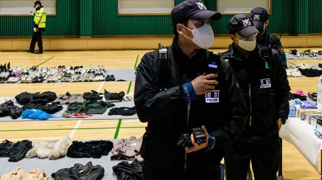 Petugas kepolisian berjalan di antara barang-barang pribadi para korban yang diambil dari tempat kejadian Tragedi Itaewon dan ditampilkan di sebuah gimnasium di Seoul, Korea Selatan, Selasa (1/11/2022). [Anthony WALLACE / AFP]
