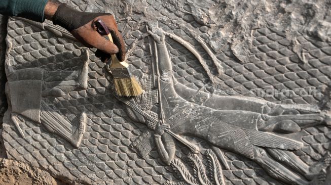 Seorang pekerja menggali relief pahatan batu yang baru-baru ini ditemukan di Gerbang Mashki, Kota Mosul, Irak, Rabu (19/10/2022). [Zaid AL-OBEIDI / AFP]
