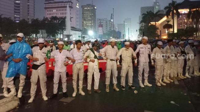 Sejumlah laskar menjaga massa GNPR saat menggelar salat Magrib berjemaah di kawasan Patung Kuda, Jakarta. (Suara.com/Rakha)