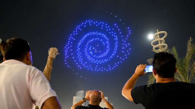  Orang-orang melihat pertunjukan drone di Lusail, Qatar, Sabtu (5/11/2022). [Kirill KUDRYAVTSEV / AFP]