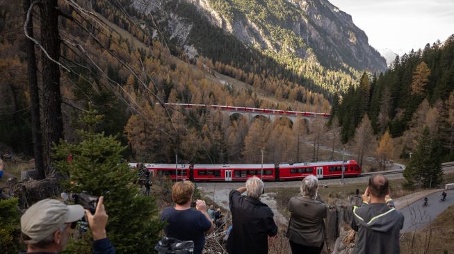 Warga mengambil gambar kereta api sepanjang 1910 meter dengan 100 gerbong saat melintas di dekat Bergun, Swiss, Sabtu (29/10/2022). [Fabrice COFFRINI / AFP]
