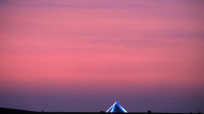 Pemandangan matahari terbenam di stan foto berbentuk piramida karya seniman Prancis JR, saat pameran Art D'Égypte "Forever is Now" di komplek Piramida Giza, Mesir, Sabtu (29/10/2022). [PATRICK BAZ / ART DEGYPTE / AFP]