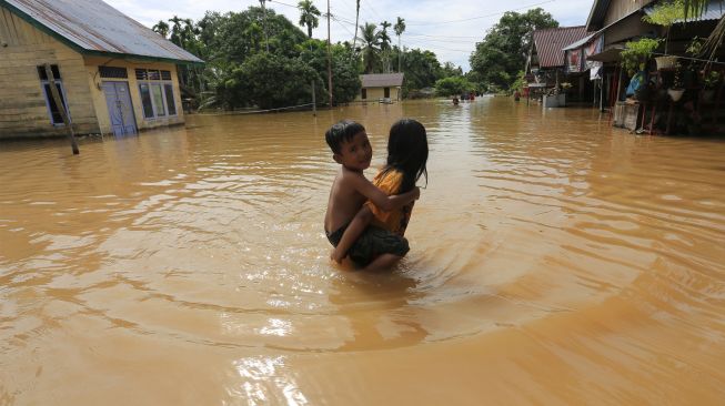 Anak-anak berjalan di depan rumahnya yang terendam banjir di Desa Napai, Woyla Barat, Aceh Barat, Aceh, Sabtu (5/11/2022). [ANTARA FOTO/Syifa Yulinnas/wsj]
