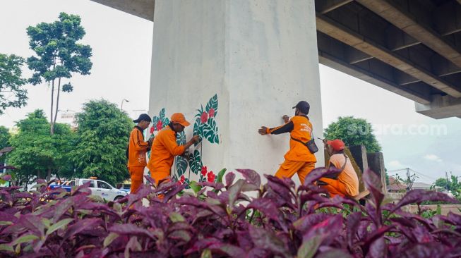 Petugas pasukan oranye wilayah Cipinang Melayu membuat mural motif bunga di kolong jalan tol Becakayu, Jatiwaringin, Jakarta Timur, Selasa (8/11/2022). [Suara.com/Alfian Winanto]