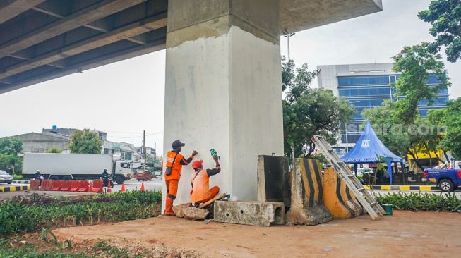 Petugas pasukan oranye wilayah Cipinang Melayu membuat mural motif bunga di kolong jalan tol Becakayu, Jatiwaringin, Jakarta Timur, Selasa (8/11/2022). [Suara.com/Alfian Winanto]