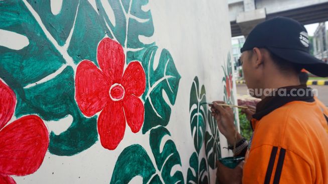 Petugas pasukan oranye wilayah Cipinang Melayu membuat mural motif bunga di kolong jalan tol Becakayu, Jatiwaringin, Jakarta Timur, Selasa (8/11/2022). [Suara.com/Alfian Winanto]