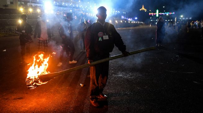 Seorang warga memegang obor yang menyala saat ia melepaskan balon udara panas dengan kembang api selama Festival Cahaya Tazaungdaing di Pyin Oo Lwin, Mandalay, Myanmar, Minggu (6/11/2022). [AFP]
