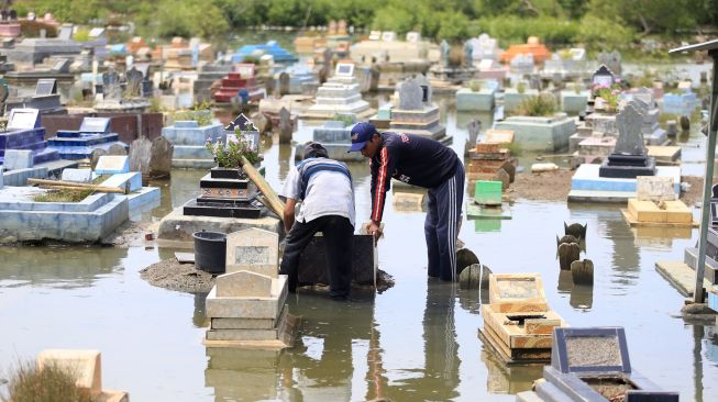 Dua warga memperbaiki makam kerabatnya yang rusak akibat terendam rob di Desa Eretan Wetan, Kandanghaur, Indramayu, Jawa Barat, Rabu (9/11/2022). [NTARA FOTO/Dedhez Anggara/YU]