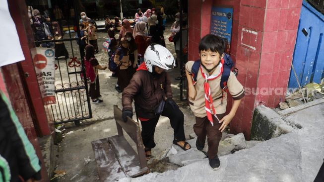 Sejumlah siswa berjalan keluar melintasi jalan darurat yang dibuat pihak orang tua murid di SDN Pondok Cina 1, Depok, Jawa Barat, Rabu (9/11/2022). [Suara.com/Alfian Winanto]