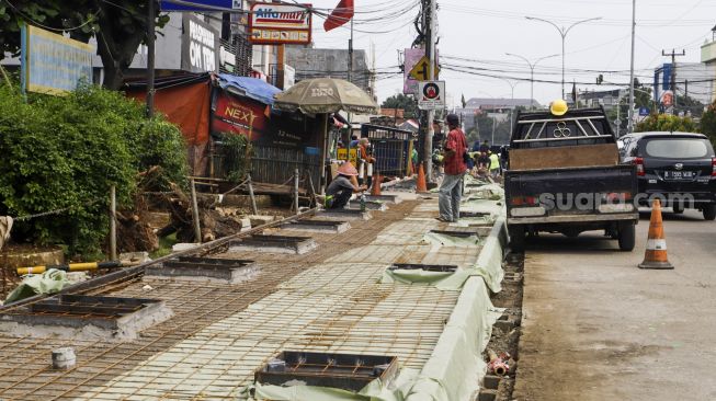 Pekerja menyelesaikan proyek revitalisasi trotoar di Jalan Dewi Sartika, Depok, Jawa barat, Rabu (9/11/2022). [Suara.com/Alfian Winanto]