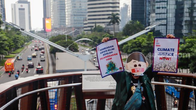 Aktivis Extinction Rebellion Indonesia (XR Indonesia) dan Walhi Jakarta melakukan aksi dengan membentangkan spanduk berisi kalimat sindiran untuk pelaksanaan KTT G20 di JPO Pinisi, Jakarta Pusat, Senin (14/11/2022). [Suara.com/Alfian Winanto]