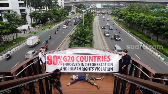 Aktivis Extinction Rebellion Indonesia (XR Indonesia) dan Walhi Jakarta melakukan aksi dengan membentangkan spanduk berisi kalimat sindiran untuk pelaksanaan KTT G20 di JPO Pinisi, Jakarta Pusat, Senin (14/11/2022). [Suara.com/Alfian Winanto]