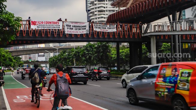 Aktivis Extinction Rebellion Indonesia (XR Indonesia) dan Walhi Jakarta melakukan aksi dengan membentangkan spanduk berisi kalimat sindiran untuk pelaksanaan KTT G20 di JPO Pinisi, Jakarta Pusat, Senin (14/11/2022). [Suara.com/Alfian Winanto]