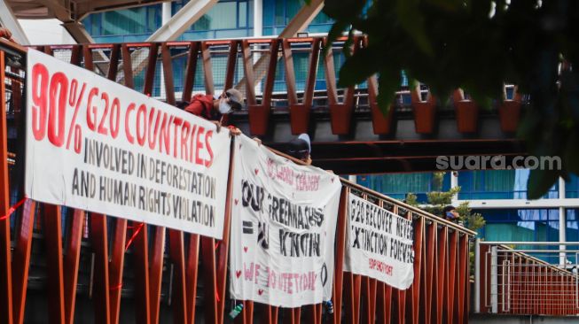 Aktivis Extinction Rebellion Indonesia (XR Indonesia) dan Walhi Jakarta melakukan aksi dengan membentangkan spanduk berisi kalimat sindiran untuk pelaksanaan KTT G20 di JPO Pinisi, Jakarta Pusat, Senin (14/11/2022). [Suara.com/Alfian Winanto]