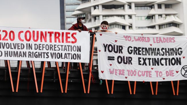 Aktivis Extinction Rebellion Indonesia (XR Indonesia) dan Walhi Jakarta melakukan aksi dengan membentangkan spanduk berisi kalimat sindiran untuk pelaksanaan KTT G20 di JPO Pinisi, Jakarta Pusat, Senin (14/11/2022). [Suara.com/Alfian Winanto]