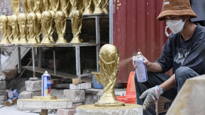 Para pekerja menyemprotkan cat emas pada model plester trofi Piala Dunia di sebuah lokakarya di Hanoi, Vietnam, Rabu (16/11/2022). [Nhac NGUYEN / AFP]