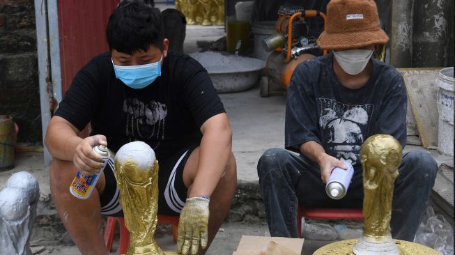 Para pekerja menyemprotkan cat emas pada model plester trofi Piala Dunia di sebuah lokakarya di Hanoi, Vietnam, Rabu (16/11/2022). [Nhac NGUYEN / AFP]
