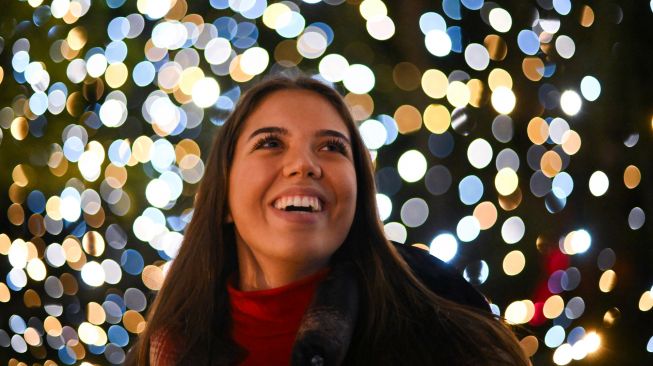 Pengunjung berpose di bawah instalasi cahaya saat perayaan natal Kew atau "Christmas at Kew" di Kew Gardens, barat daya London, Inggris, Selasa (15/11/2022). [Daniel LEAL / AFP]