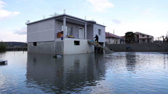 Seorang warga memasuki rumahnya yang terendam banjir di desa Kuc dekat kota Shkodra, Albania, Senin (21/11/2022). [Gent SHKULLAKU / AFP]
