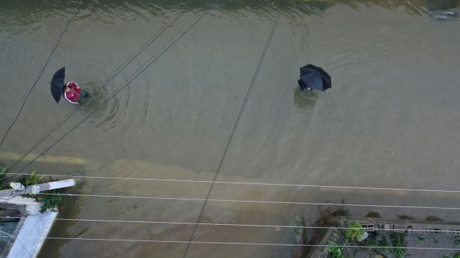 Warga berjalan di antara rumah-rumah yang terendam banjir di Shkodra, Albania, Senin (21/11/2022). [Gent SHKULLAKU / AFP]
