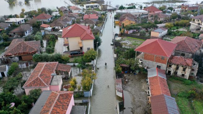 Warga berjalan di antara rumah-rumah yang terendam banjir di Shkodra, Albania, Senin (21/11/2022). [Gent SHKULLAKU / AFP]