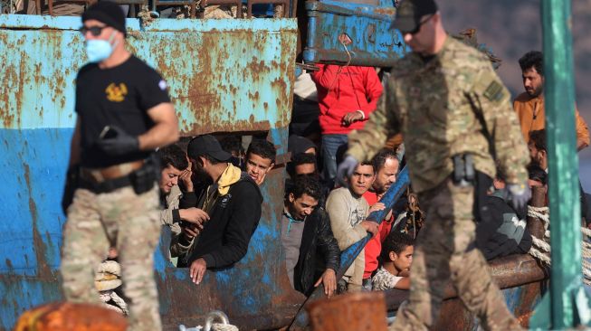 Pengungsi dan migran yang diselamatkan berdiri di atas kapal setelah opreasi penyelamatan di kota Paleochora, Pulau Kreta, Yunani, Selasa (22/11/2022). [Costas METAXAKIS / AFP]