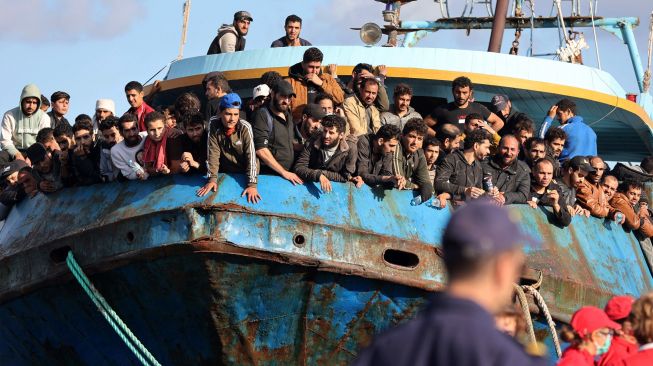 Pengungsi dan migran yang diselamatkan berdiri di atas kapal setelah opreasi penyelamatan di kota Paleochora, Pulau Kreta, Yunani, Selasa (22/11/2022). [Costas METAXAKIS / AFP]
