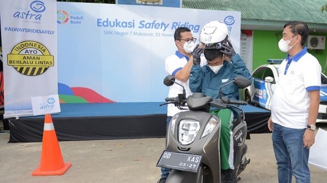 Director Asuransi Astra, Mulia K. B. Siregar dan Adi Sepiarso membantu pemakaian safety kit kepada murid saat edukasi safety riding di SMKN 7 Makassar [Asuransi Astra].