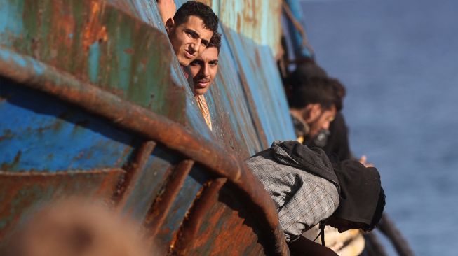 Pengungsi dan migran yang diselamatkan berdiri di atas kapal setelah opreasi penyelamatan di kota Paleochora, Pulau Kreta, Yunani, Selasa (22/11/2022). [Costas METAXAKIS / AFP]
