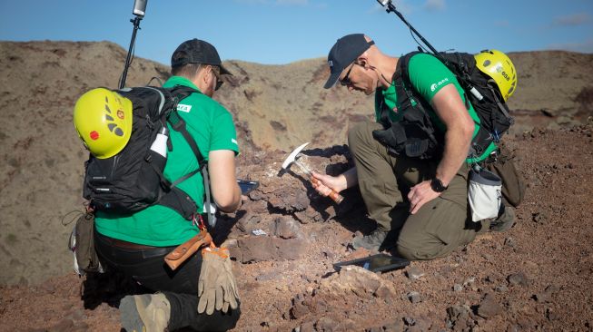 Astronot Jerman Alexander Gerst (kanan) mengumpulkan bebatuan di puncak gunung berapi purba selama program pelatihan untuk mempelajari cara menjelajahi Bulan dan Mars di Taman Nasional Timanfaya Pulau Lanzarote, Kepulauan Canary, Spanyol, Selasa (10/11/2022). [DESIREE MARTIN / AFP]
