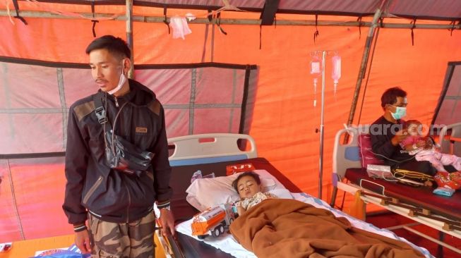 Azka (5), seorang anak yang selamat dari reruntuhan puing rumahnya, akibat gempa Cianjur, hanya bisa terbaring di atas kasur rumah sakit dalam tenda darurat di halaman Rumah Sakit Umum Daerah Sayang Cianjur. (Suara.com/Faqih)