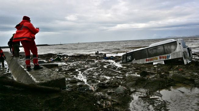 Seorang pria berjalan melewati mobil yang rusak akibat hujan lebat yang memicu tanah longsor di pulau Ischia selatan, Italia, Sabtu (26/11/2022). [ANSA / Ansa / Italy OUT / AFP]