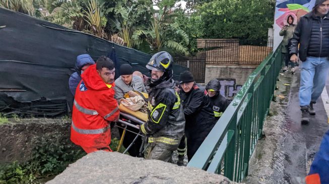 Petugas pemadam kebakaran Italia mengevakuasi seorang pria keluar dari rumahnya di Casamicciola, Pulau Ischia selatan, Italia, Sabtu (26/11/2022). [ANSA / Ansa / Italy OUT / AFP]