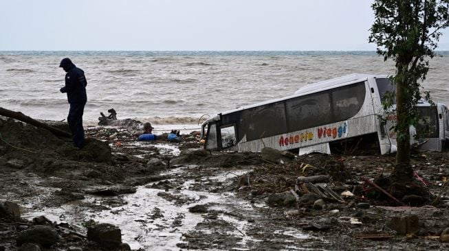 Seorang pria berjalan melewati mobil yang rusak akibat hujan lebat yang memicu tanah longsor di pulau Ischia selatan, Italia, Sabtu (26/11/2022). [ANSA / Ansa / Italy OUT / AFP]