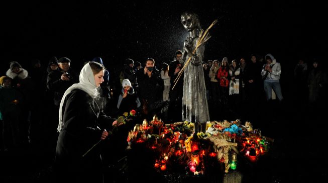 Seorang penduduk setempat meletakkan bunga saat upacara di monumen para korban Holodomor di Kyiv, Ukraina, Sabtu (26/11/2022). [Sergei CHUZAVKOV / AFP]
