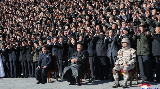 Pemimpin Korea Utara Kim Jong Un (duduk di tengah) dan putrinya (berdiri di tengah) foto bersama dengan para ilmuwan, insinyur, pejabat militer dan para pekerja di pabrik amunisi yang berkontribusi dalam uji coba rudal balistik antarbenua (ICBM) Hwasong-17 di lokasi rahasia, dalam foto tak bertanggal yang rilis pada Minggu (27/11/2022). [KCNA VIA KNS / AFP]