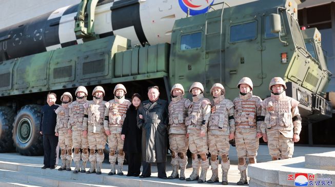 Pemimpin Korea Utara Kim Jong Un (tengah kanan) dan putrinya (tengah kiri) berpose dengan tentara yang berkontribusi dalam uji coba rudal balistik antarbenua (ICBM) Hwasong-17 di lokasi rahasia, dalam foto tak bertanggal yang rilis pada Minggu (27/11/2022). [KCNA VIA KNS / AFP]