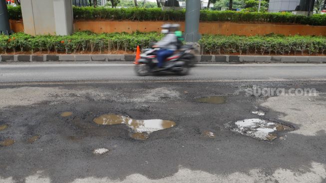 Kendaraan melintasi jalan rusak di sekitar Pembangunan Stasiun LRT, Jalan Rasuna Said, Jakarta Selatan, Rabu (30/11/2022). [Suara.com/Alfian Winanto]