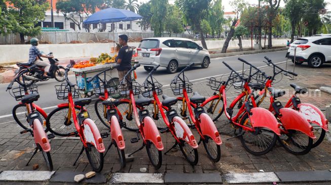 Warga melintas melintas di dekat sepeda sewa yang terparkir di Pasar Baru, Jakarta Pusat, Rabu (30/11/2022). [Suara.com/Alfian Winanto]