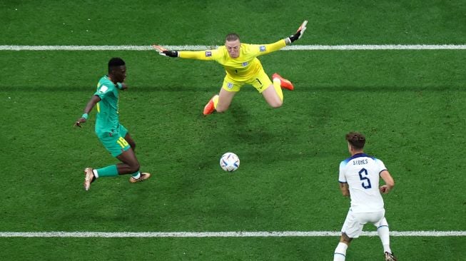 Kiper Inggris Jordan Pickford bersiap untuk menghentikan bola yang ditembakkan oleh penyerang Senegal Ismaila Sarr (kiri) saat pertandingan sepak bola babak 16 besar Piala Dunia 2022 antara Inggris dan Senegal di Stadion Al-Bayt di Al Khor, utara Doha, Qatar, Minggu (4/12/2022). [Giuseppe CACACE/AFP]
