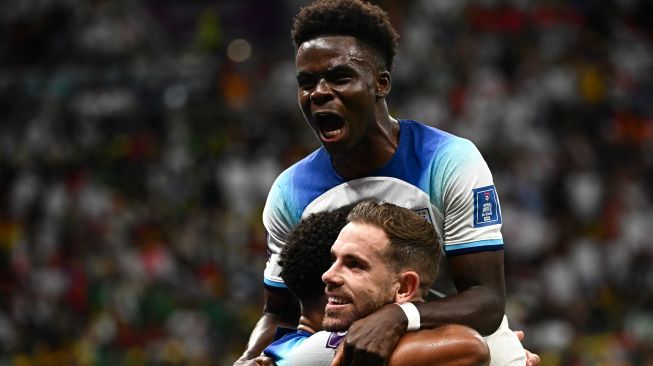 Gelandang Inggris Jordan Henderson (bawah) merayakan dengan penyerang Inggris Bukayo Saka setelah  mencetak gol saat pertandingan sepak bola babak 16 besar Piala Dunia 2022 antara Inggris dan Senegal di Stadion Al-Bayt di Al Khor, utara Doha, Qatar, Minggu (4/12/2022). [Anne-Christine POUJOULAT / AFP]