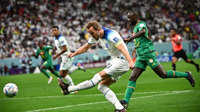 Penyerang Inggris Harry Kane menendang bola saat pertandingan sepak bola babak 16 besar Piala Dunia 2022 antara Inggris dan Senegal di Stadion Al-Bayt di Al Khor, utara Doha, Qatar, Minggu (4/12/2022). [Anne-Christine POUJOULAT / AFP]