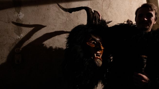 Orang-orang bersiap untuk mengenakan topeng setan dan kulit domba hitam yang mewakili Krampus, penolong Santo Nikolas saat menghadiri parade Santo Nikolas (Nikolospiel) di Bad Mitterndorf, Styria, Austria, Senin (5/12/2022). [JOE KLAMAR / AFP]