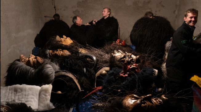 Orang-orang bersiap untuk mengenakan topeng setan dan kulit domba hitam yang mewakili Krampus, penolong Santo Nikolas saat menghadiri parade Santo Nikolas (Nikolospiel) di Bad Mitterndorf, Styria, Austria, Senin (5/12/2022). [JOE KLAMAR / AFP]