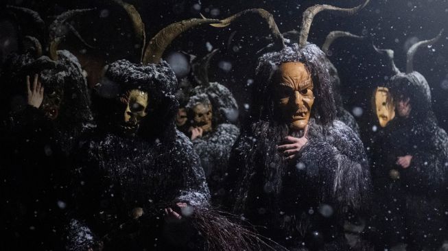 Orang-orang mengenakan topeng setan dan kulit domba hitam yang mewakili Krampus, penolong Santo Nikolas saat menghadiri parade Santo Nikolas (Nikolospiel) di Bad Mitterndorf, Styria, Austria, Senin (5/12/2022). [JOE KLAMAR / AFP]