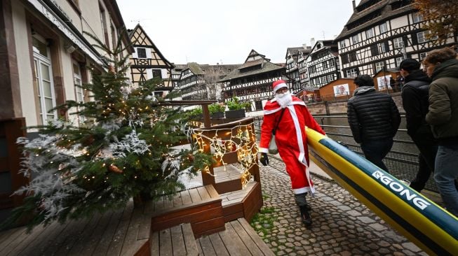 Seorang pendayung berpakaian Sinterklas membawa papan dayung saat menghadiri parade SUP (Stand Up Paddleboarding) sungai Ill di Strasbourg, Prancis, Sabtu (3/12/2022). [SEBASTIEN BOZON/AFP]