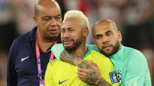 Penyerang Brazil Neymar menangis dan dihibur oleh bek Brazil Dani Alves setelah tim mereka kalah dalam pertandingan sepak bola perempat final Piala Dunia 2022 antara Kroasia dan Brazil di Stadion Education City di Al-Rayyan, barat Doha, Qatar, Jumat (9/12/2022). [Adrian DENNIS/AFP]