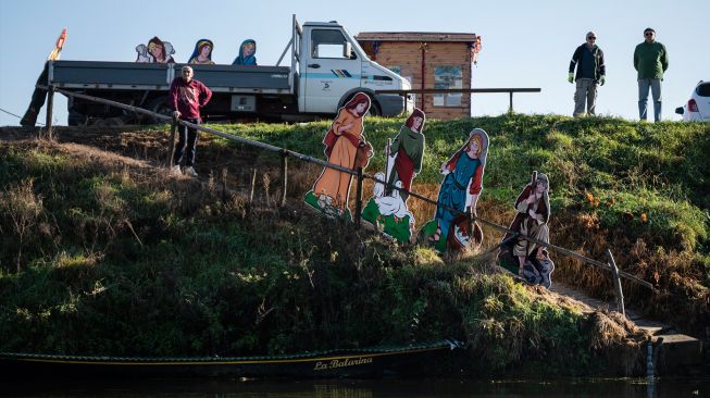 Warga saat akan memasang Instalasi Natal yang berkisah tentang kelahiran Yesus di sungai Po, Villafranca Piemonte, Turin, Italia, Selasa (6/12/2022). [MARCO BERTORELLO / AFP]
