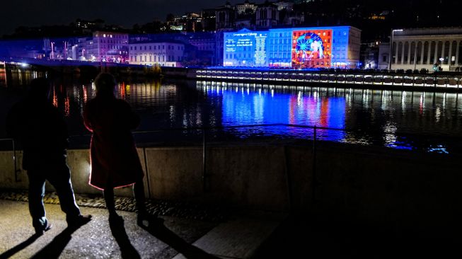 Pejalan kaki menyaksikan Notre-Dame de Fourviere basilica yang diterangi cahaya dalam acara tahunan Festival Cahaya (Fete des Lumieres) di Lyon, Prancis, Rabu (7/12/2022). [OLIVIER CHASSIGNOLE / AFP]
