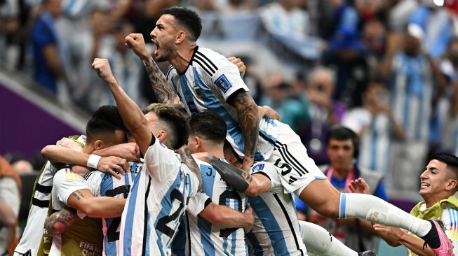 Gelandang Argentina Leandro Paredes melompati rekan satu timnya saat mereka selebrasi ketika pemain depan Argentina Lionel Messi mencetak gol saat pertandingan sepak bola perempat final Piala Dunia 2022 antara Belanda dan Argentina di Stadion Lusail, utara Doha, Qatar, Jumat (9/12/2022). [MANAN VATSYAYANA/AFP]